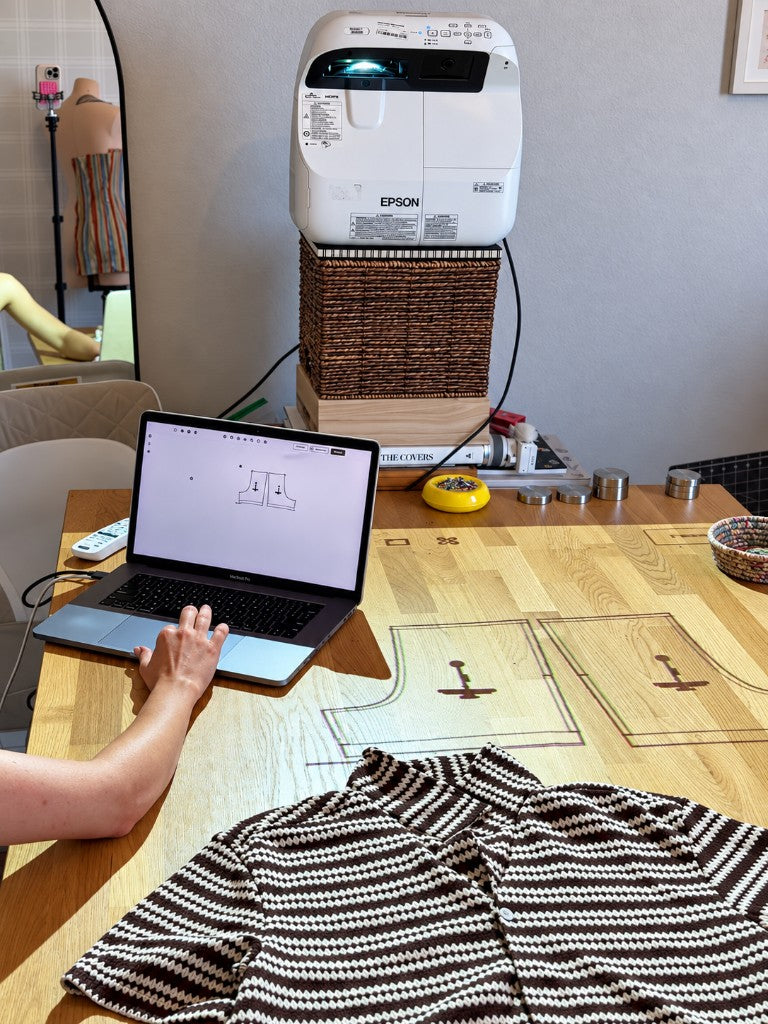 A projector and laptop showing a knit shorts pattern beside a sewn pair